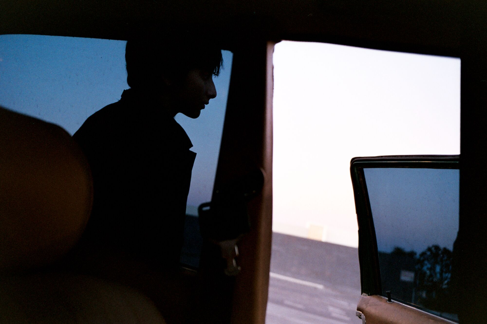 The silhouette of a person standing outside their car