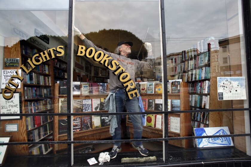 A man stands in the window of a store, leaning back with a squeegee.