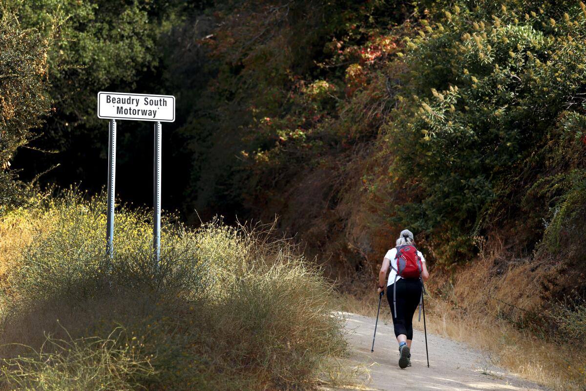 A woman walks on the Beaudry South Motorway trail in Glendale next to a sign with the trail's name.