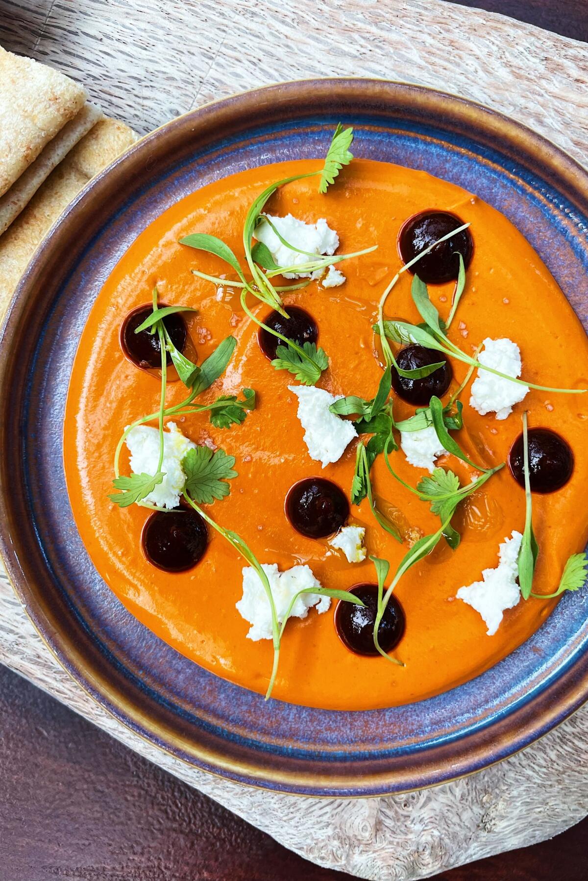 An orange dip of cashew muhammara with feta cheese and dots of ancho chile in a ceramic bowl at the Rose Venice