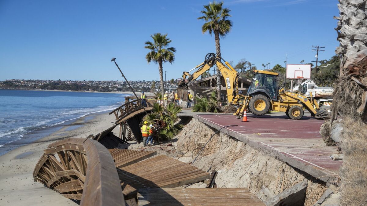 Orange County public works crews use heavy machinery to remove a damaged boardwalk at Capistrano Beach in Dana Point. Damage to coastal property is one of the greatest costs of climate change.