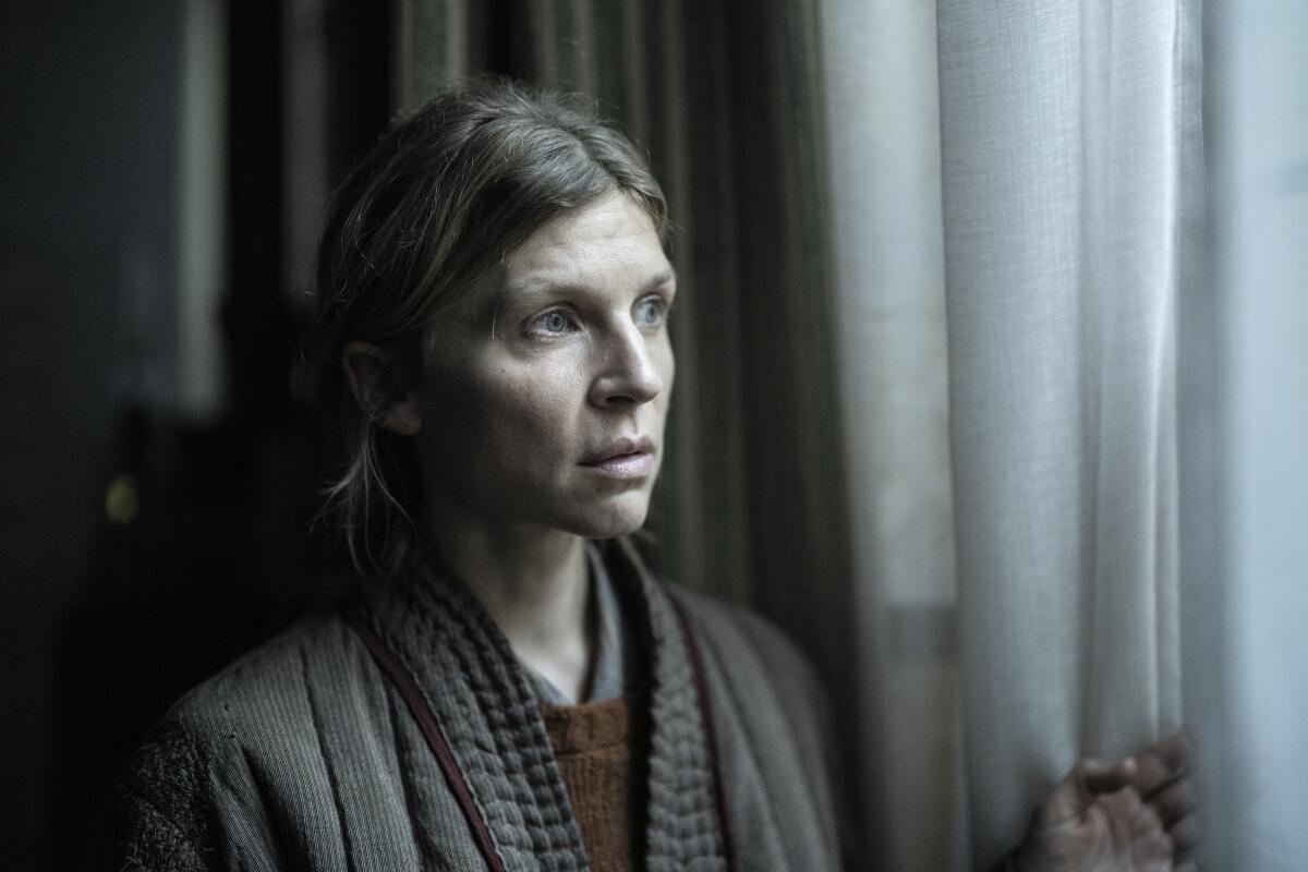 A woman (Clémence Poésy as Isabelle) parts curtains to peer apprehensively out a window in "The Walking Dead: Daryl Dixon." 