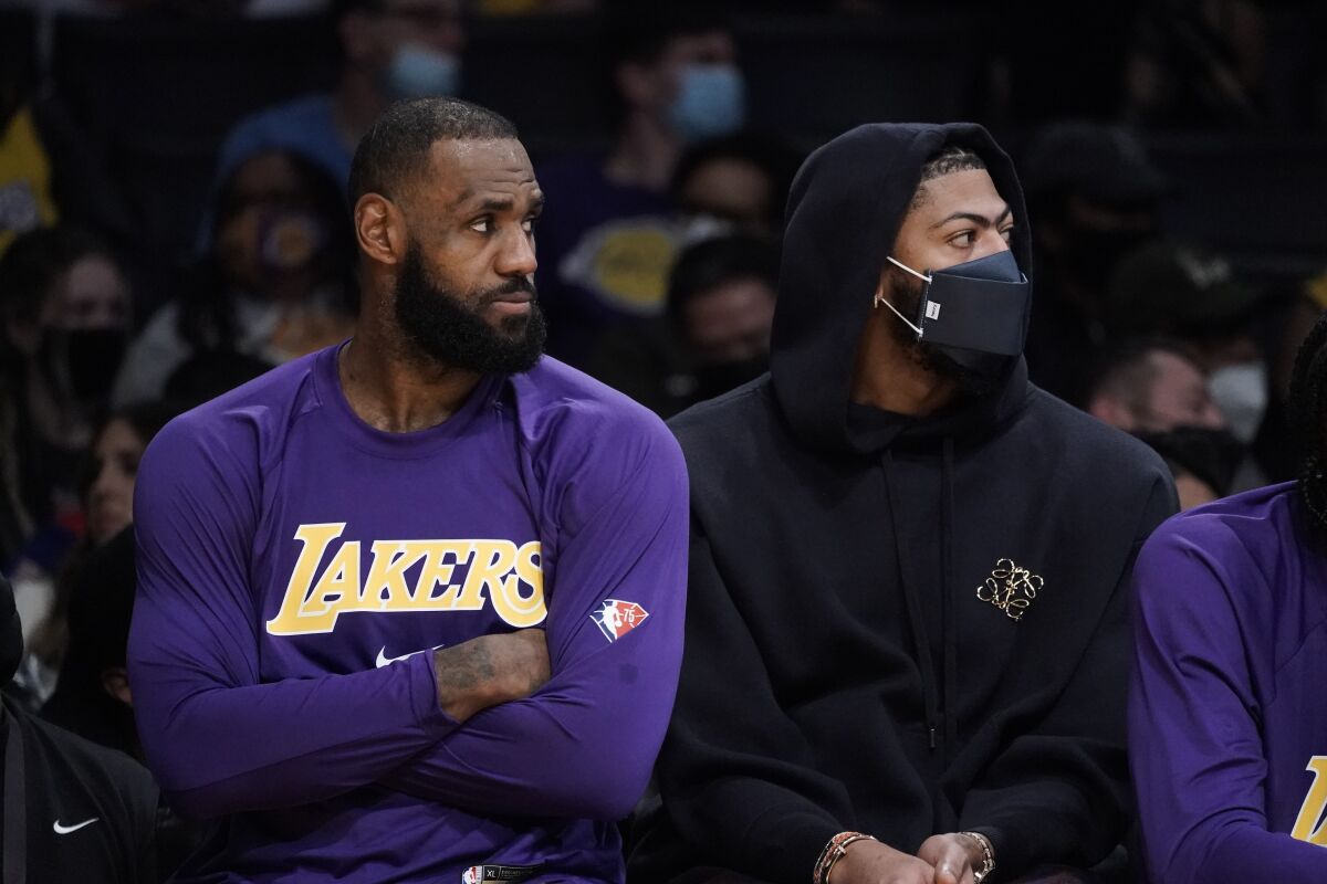 Lakers stars LeBron James, left, and Anthony Davis watch their teammates play while sitting on the bench.