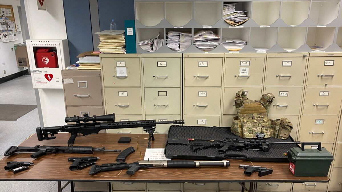 Guns and other weapons are spread out on a table in front of filing cabinets.