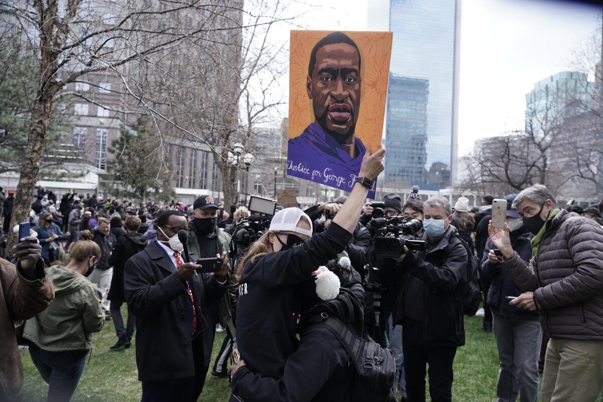Amid a crowd, a woman carries a sign with an image of George Floyd.