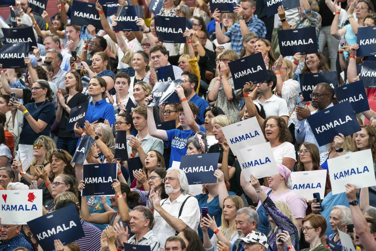 People in a crowd hold up white and blue signs that read "Kamala."