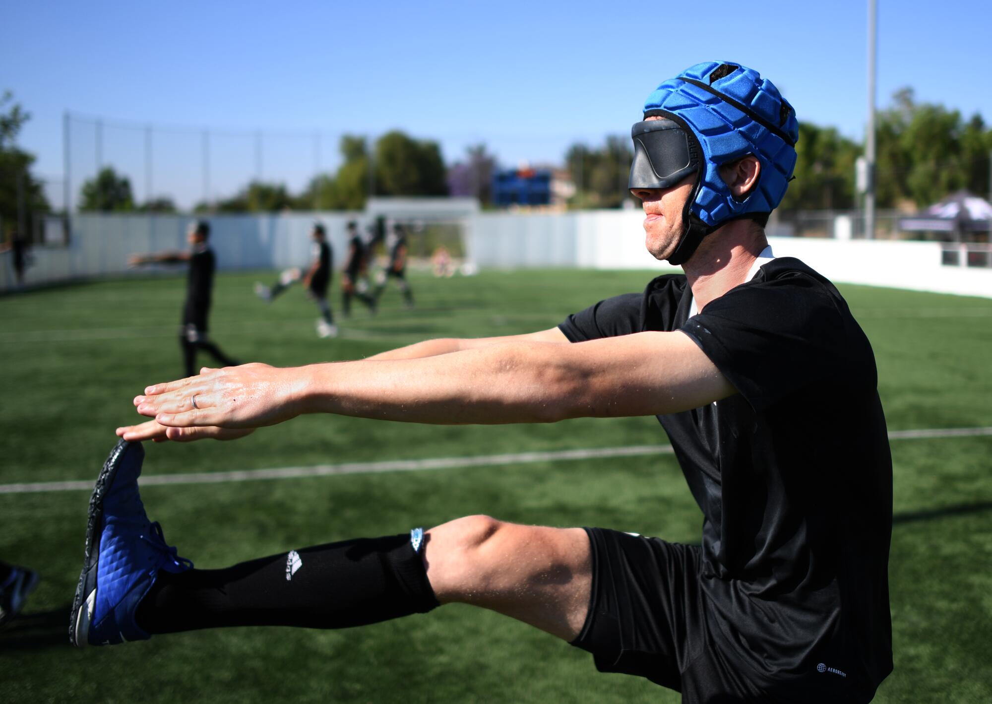 Blind soccer player Charles E. Catherine-Caldaro wears a padded helmet and goggles while extending his leg to stretch