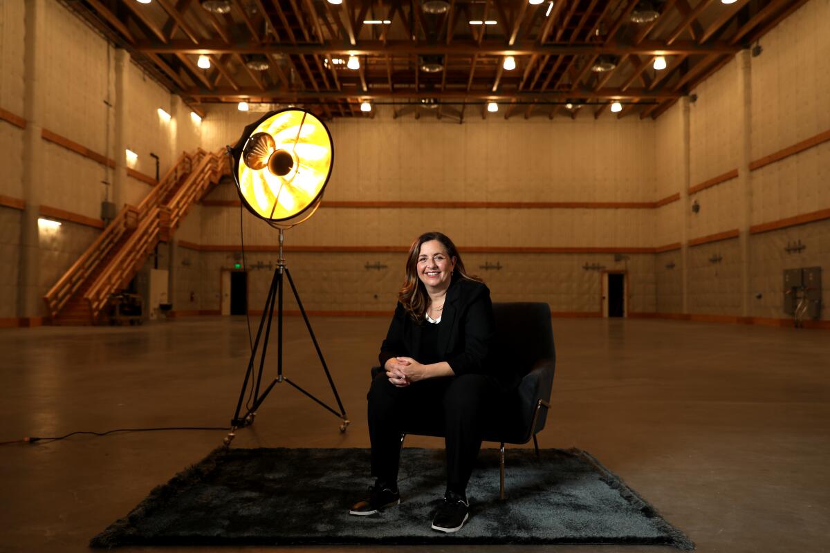 A woman sits in a chair under a lamp smiling