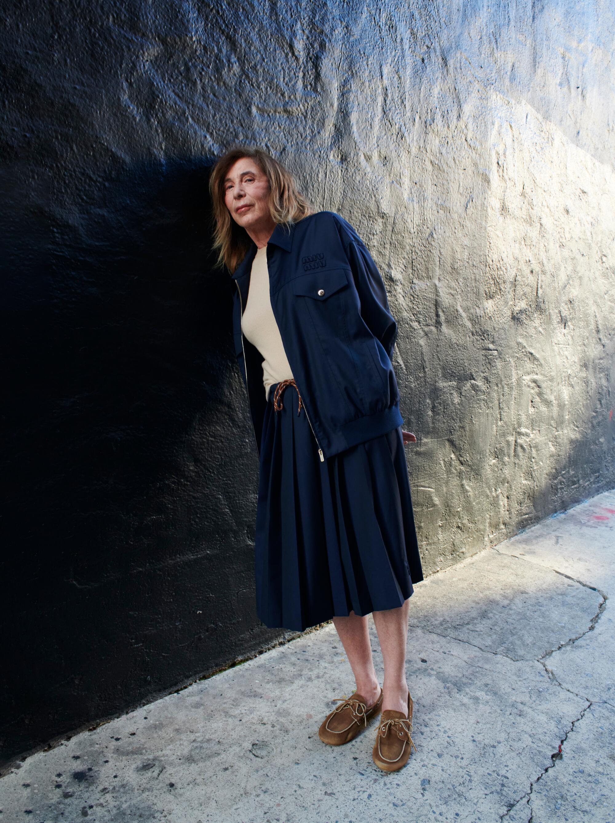 A woman leans against a black wall.