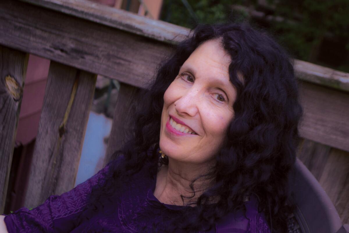 A smiling woman with dark curly hair, seated next to a wooden railing