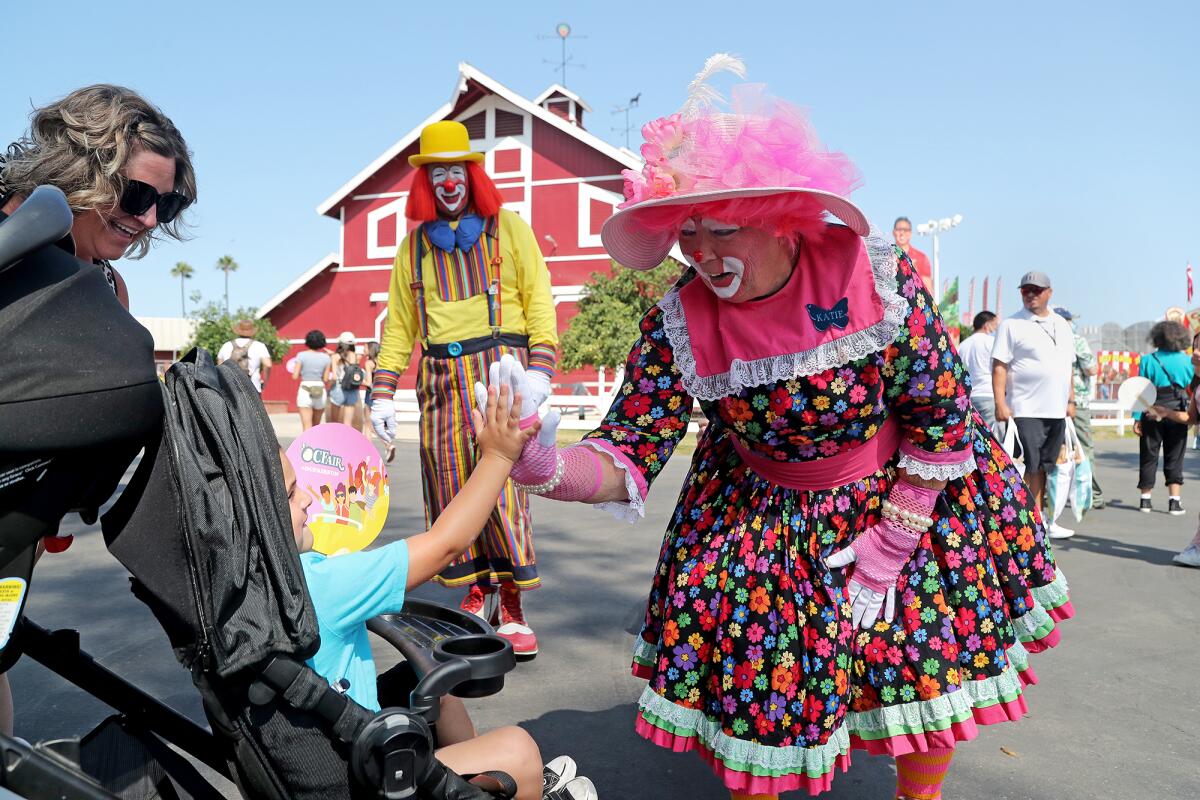 Fair clown, Katie, on Friday welcomes a young fairgoer with a high five on opening day of the O.C. Fair in Costa Mesa.