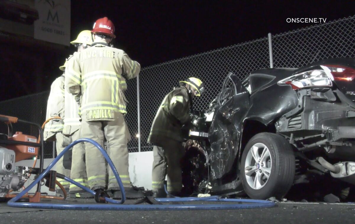 Firefighters stand on the 215 freeway by a crashed car.