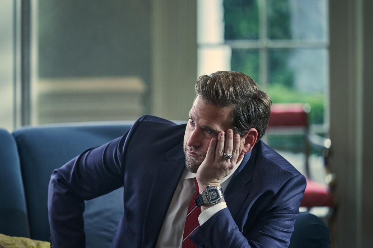 A man in a suit sits resting his head in his hand.