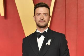 Justin Timberlake smiles in a tie and tuxedo in front of a red and yellow backdrop