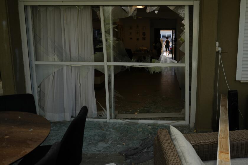 A woman stands on the doorway of a damaged house following an attack from Lebanon, in Acre, north Israel, Sunday, Aug. 25, 2024. (AP Photo/Ariel Schalit)