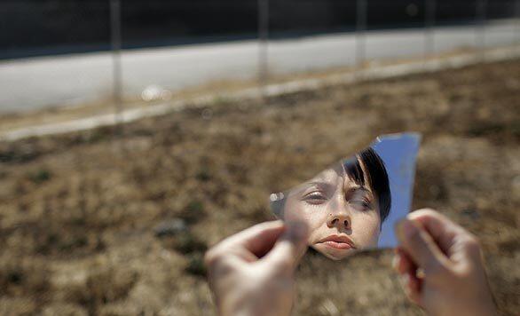 Viviana Franco stares at her reflection in a broken mirror found among the trash on the barren lot in Hawthorne 100 feet from where she grew up. She earned a masters degree in urban planning at UCLA specifically to clean up the lot and replace its hardscrabble dirt with a blanket of grass.
