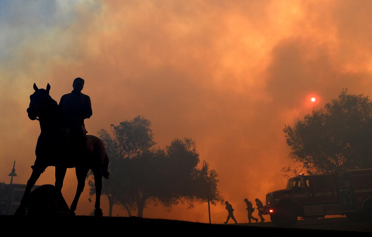 A statue of President Ronald Reagan titled "Along The Trail" stands outside the Reagan Library as the Easy Fire burns