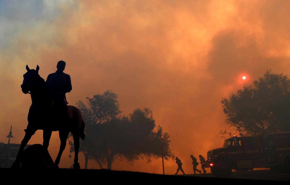 A statue of President Ronald Reagan titled "Along The Trail" stands outside the Reagan Library as the Easy Fire burns