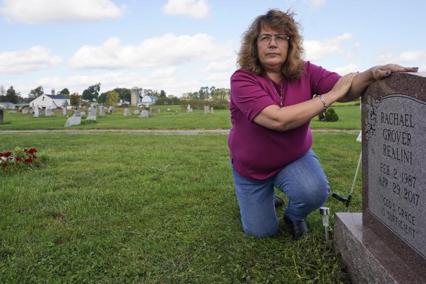 Sharon Grover rests her hands on the gravestone for her daughter, Rachael, Tuesday, Sept. 28, 2021, at Fairview Cemetery in Mesopotamia, Ohio. Grover believes her daughter started using prescription painkillers around 2013 but missed any signs of her addiction as her daughter, the oldest of five children, remained distanced. (AP Photo/Tony Dejak)