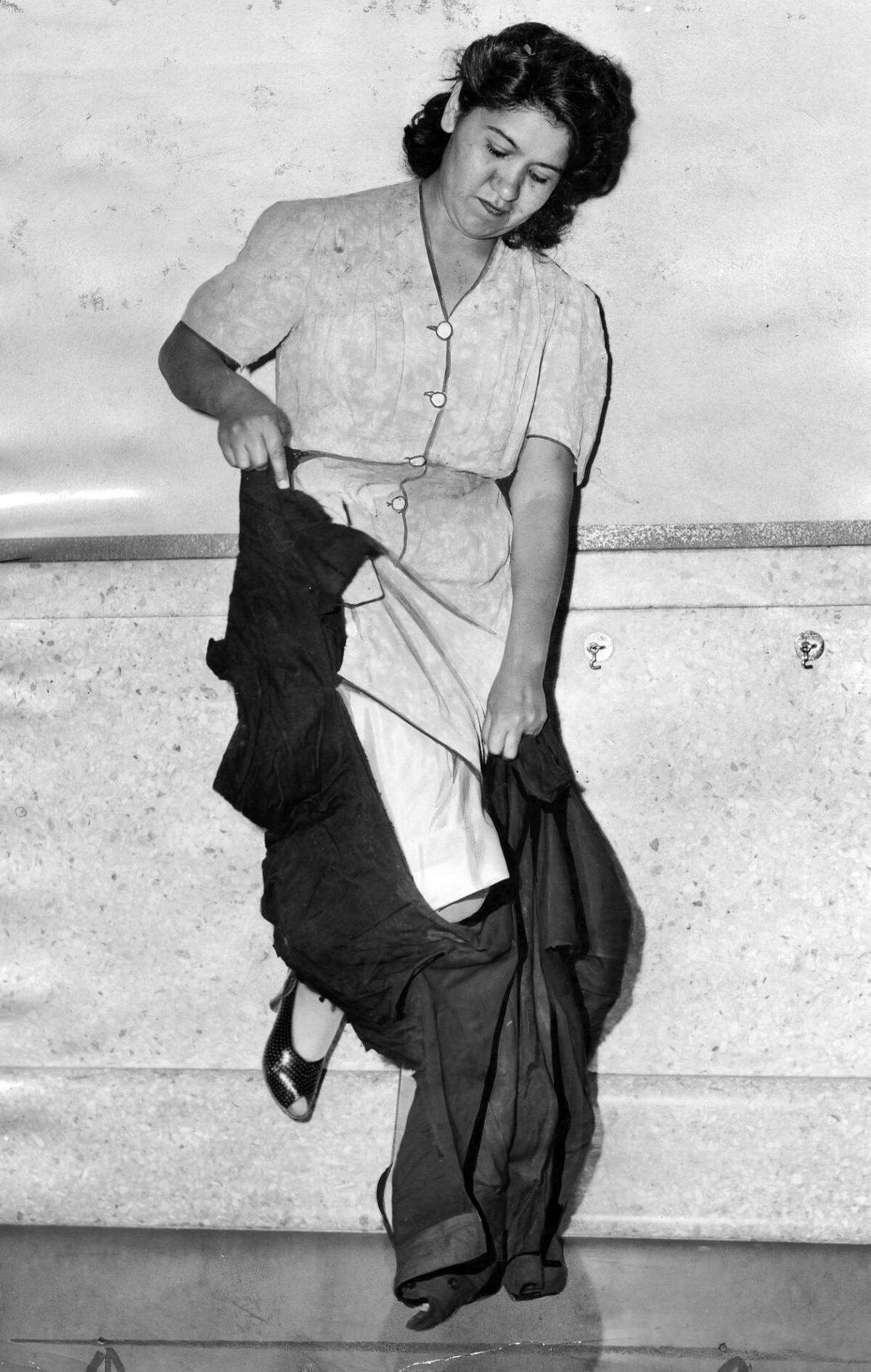 A vintage black and white news photograph shows a Latina woman tearing a zoot suit apart.
