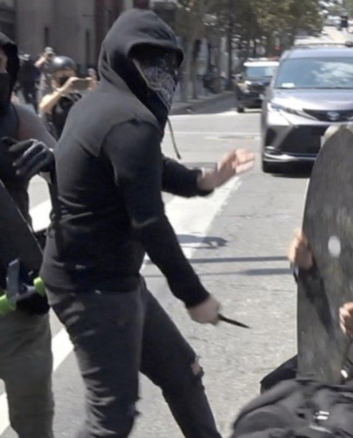 A suspect in a hoodie and bandana holds a knife.