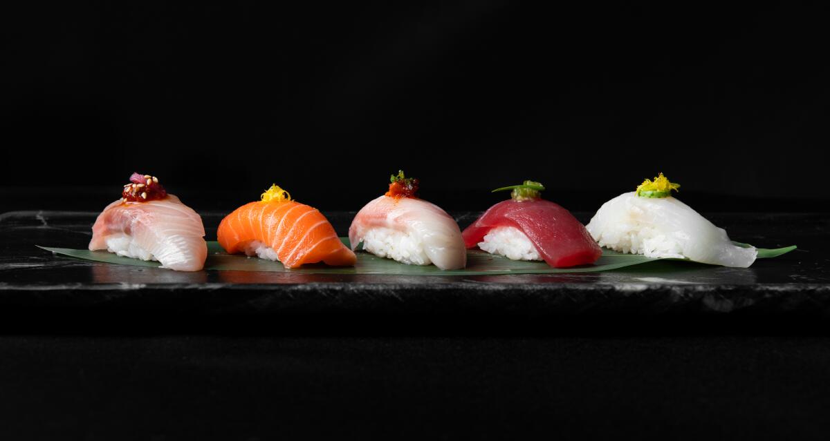 A photo of a lineup of nigiri from Fiish, each topped with a colorful garnish against a black background.