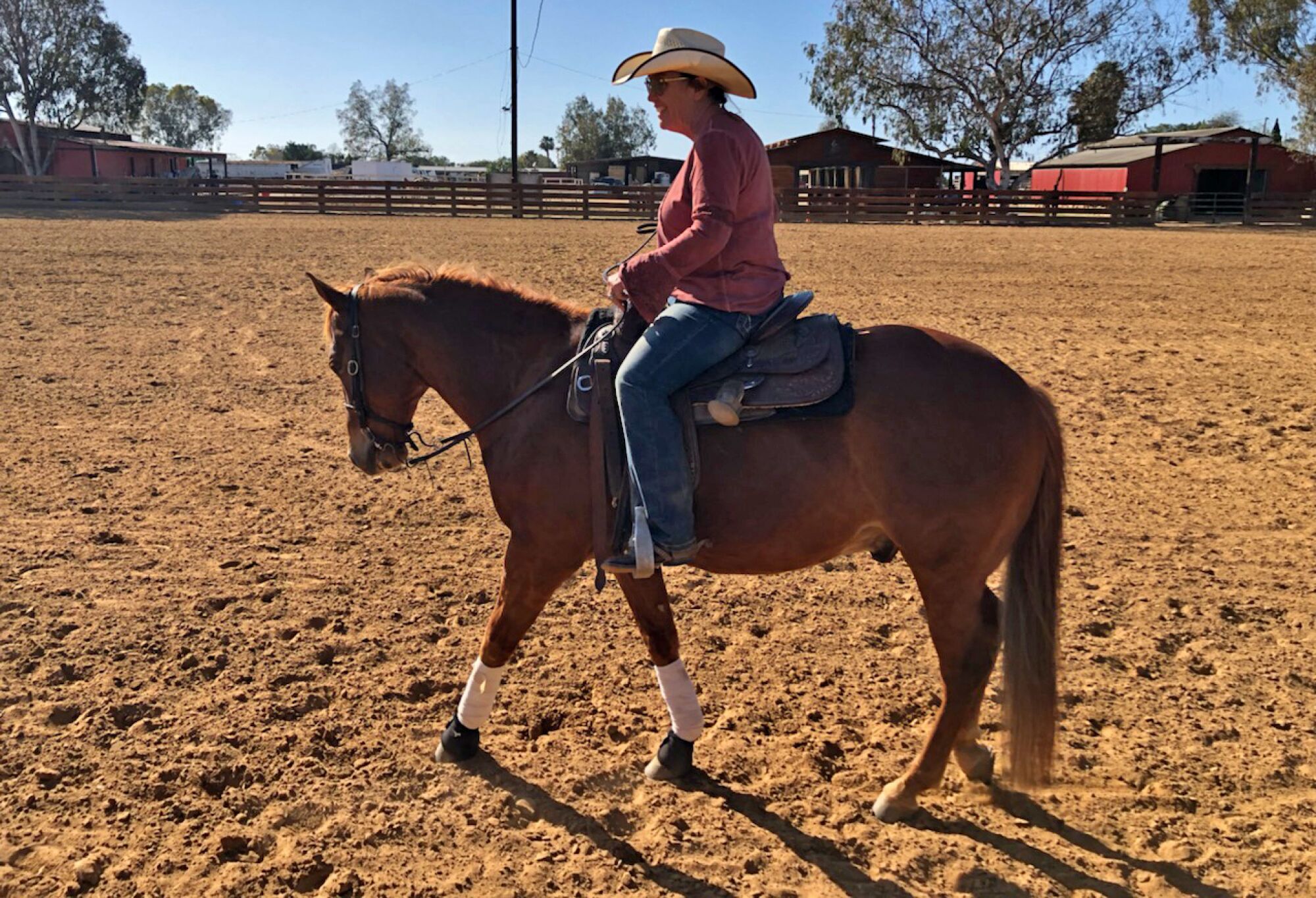 A person in a cowboy hat rides a horse in a large corral.