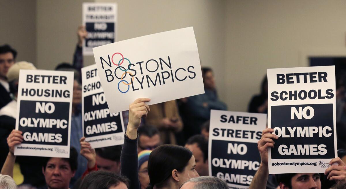 People in the audience hold up placards against the Olympic Games coming to Boston during a public forum regarding the city's 2024 Olympic bid.
