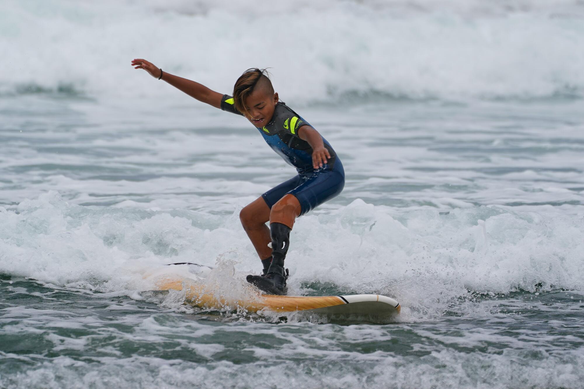 Jonah Villamil, 12, wears his 3-D printed prosthetic leg while successfully standing up on his board in the low surf.