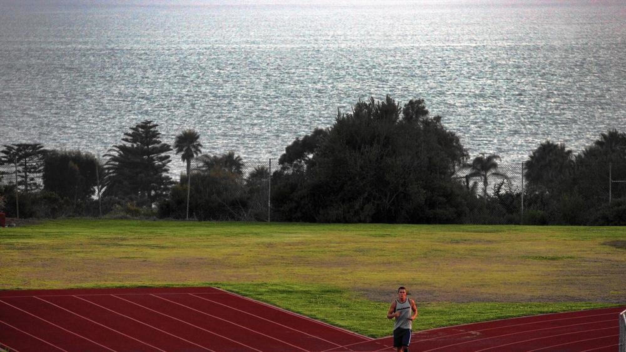 A runner on a track with the ocean in the background.
