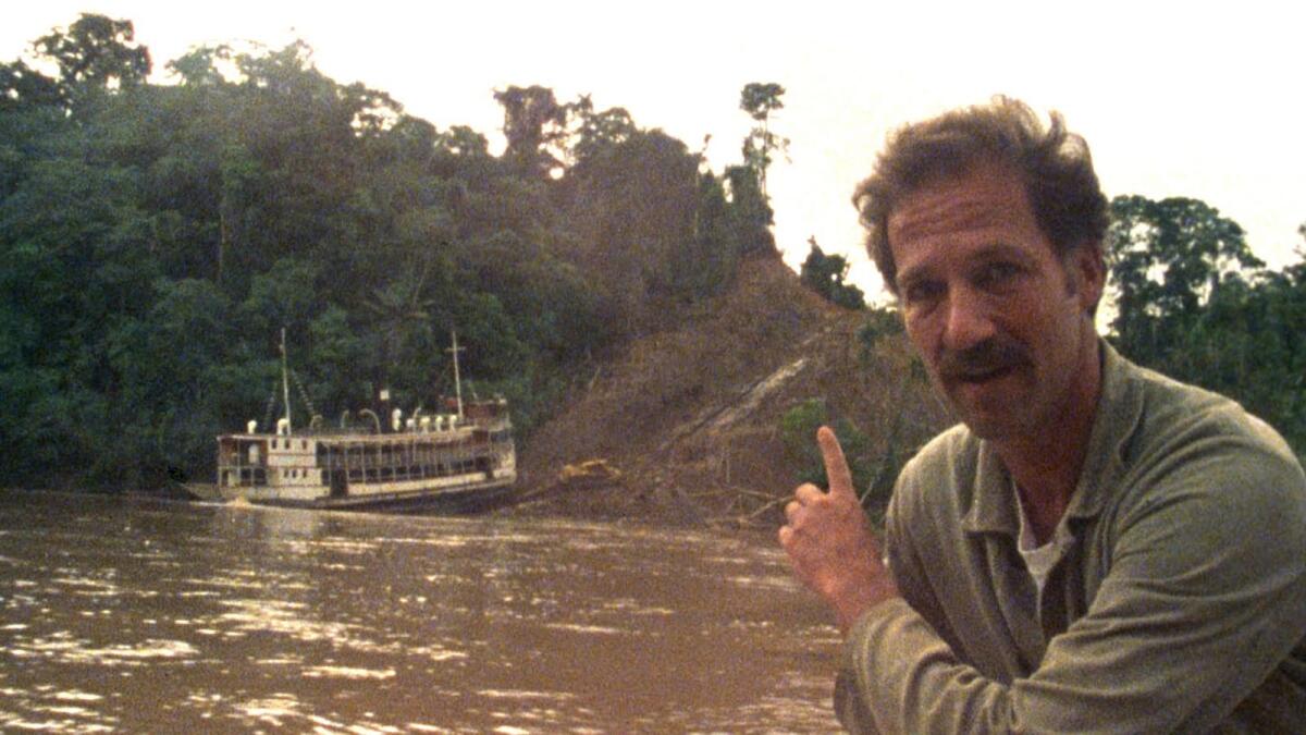 A man points something out on a river, with a boat visible on the far bank.