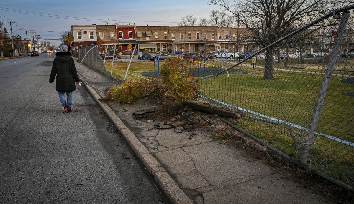 A neighborhood resident walks around a fence that was knocked down when a Baltimore Police officer was shot and crashed through the fence into Curtis Bay Park early Thursday, Dec. 16, 2021. (Jerry Jackson/The Baltimore Sun via AP)