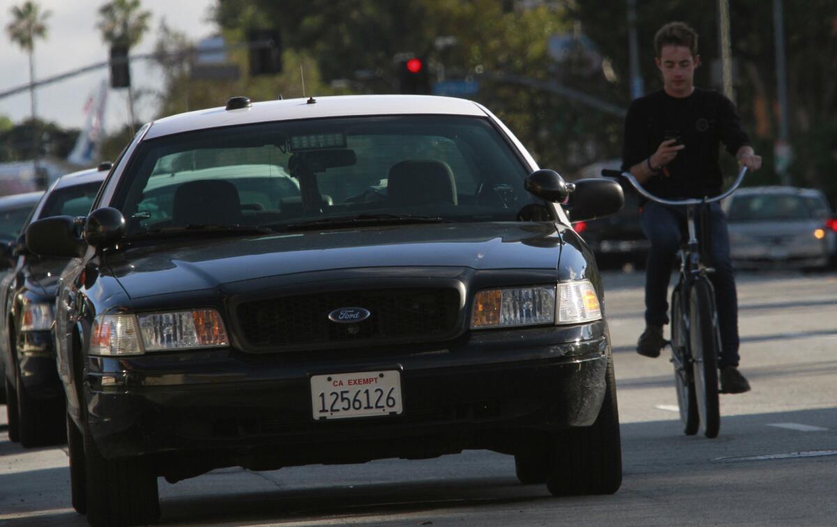 A bicyclist passes two LAPD cars parked at the corner of Figueroa and 30th streets in 2012. An investigation found that at least five of the department's patrol divisions artificially inflated the number of officers on patrol.