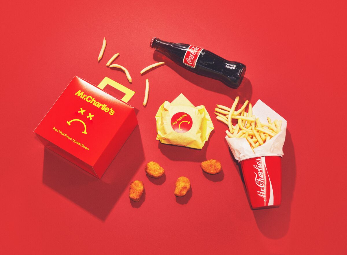 A red fast-food box, wrapped vegan burger, cup of fries and scattered vegan nuggets.