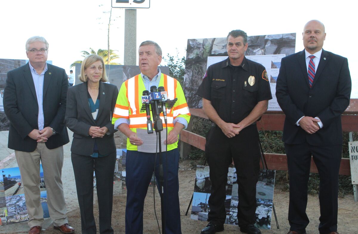 City of San Diego deputy chief operating officer Johnnie Perkins (center) announces the reopening of a stabilized Coast Boulevard on Oct. 16, flanked by Public Works Department Director James Nagelvoort, City Council member Barbara Bry, San Diego Lifeguard Chief James Gartland and Transportation and Storm Water Director Kris McFadden.<br>