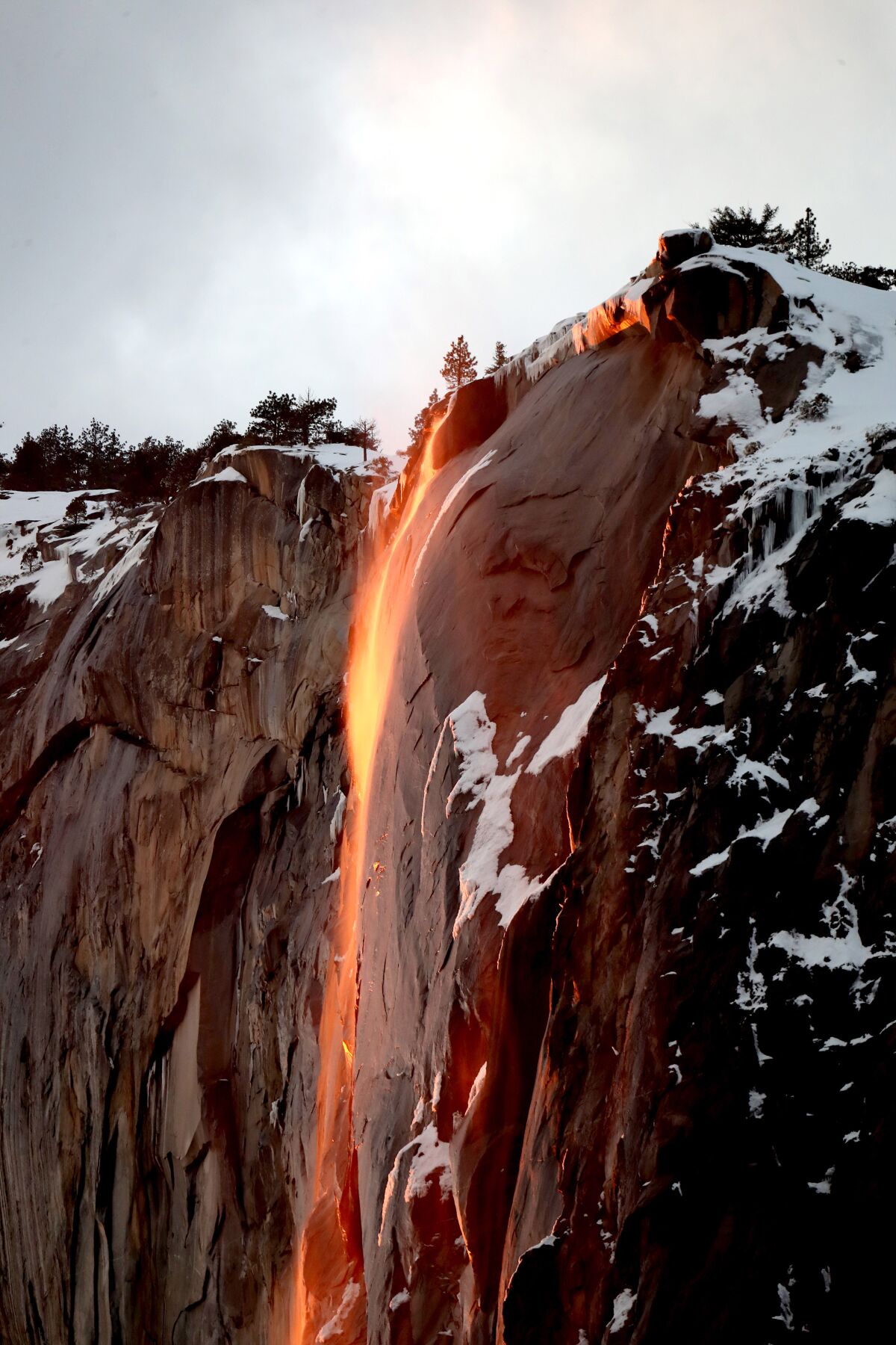 Closeup of a stream of water falling off a cliff face that glows orange and red.