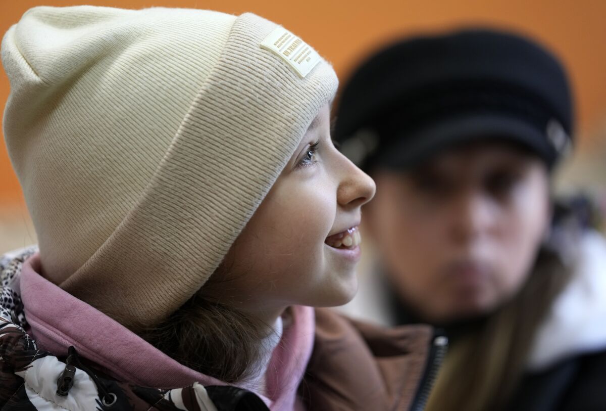 Annamaria Moslovska, a ten-year-old from Kharkiv, eastern Ukraine, smiles in a waiting room at the train station in Zahony, Hungary, Monday, March 7, 2022. After hearing bombs falling in her hometown of Kharkiv, Annamaria Maslovska left her friends, her toys, and her life in Ukraine and set off on a two-day journey with her mother to Hungary. From inside the train station at the town of Zahony, on Hungary's border with Ukraine, the 10-year-old said she is worried about her friends in Kharkiv after the messages she sent to them on Viber have gone unanswered. (AP Photo/Darko Vojinovic)