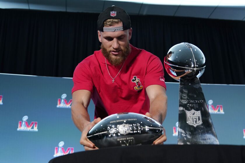 Los Angeles Rams wide receiver Cooper Kupp places the Super Bowl MVP trophy next to the Vince Lombardi.