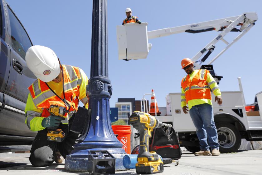 SAN DIEGO, CA - JULY 5: Contractor Israel Ruelas, left, repairs the electrical wiring on a street lamp in the East 