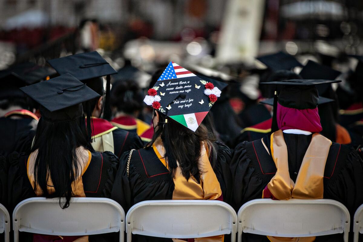 The backs of sitting people wearing black robes and mortar boards.
