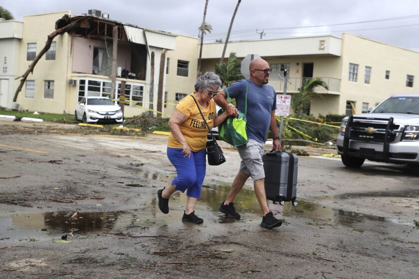 King Point resident Maria Esturilho is escorted by her son Tony Esturilho as they leave behind the damage from an apparent overnight tornado spawned from Hurricane Ian at Kings Point 55+ community in Delray Beach, Fla., on Wednesday, Sept. 28, 2022. (Carline Jean /South Florida Sun-Sentinel via AP)