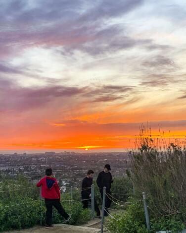 People stand on a hill watching a glowing orange sunset