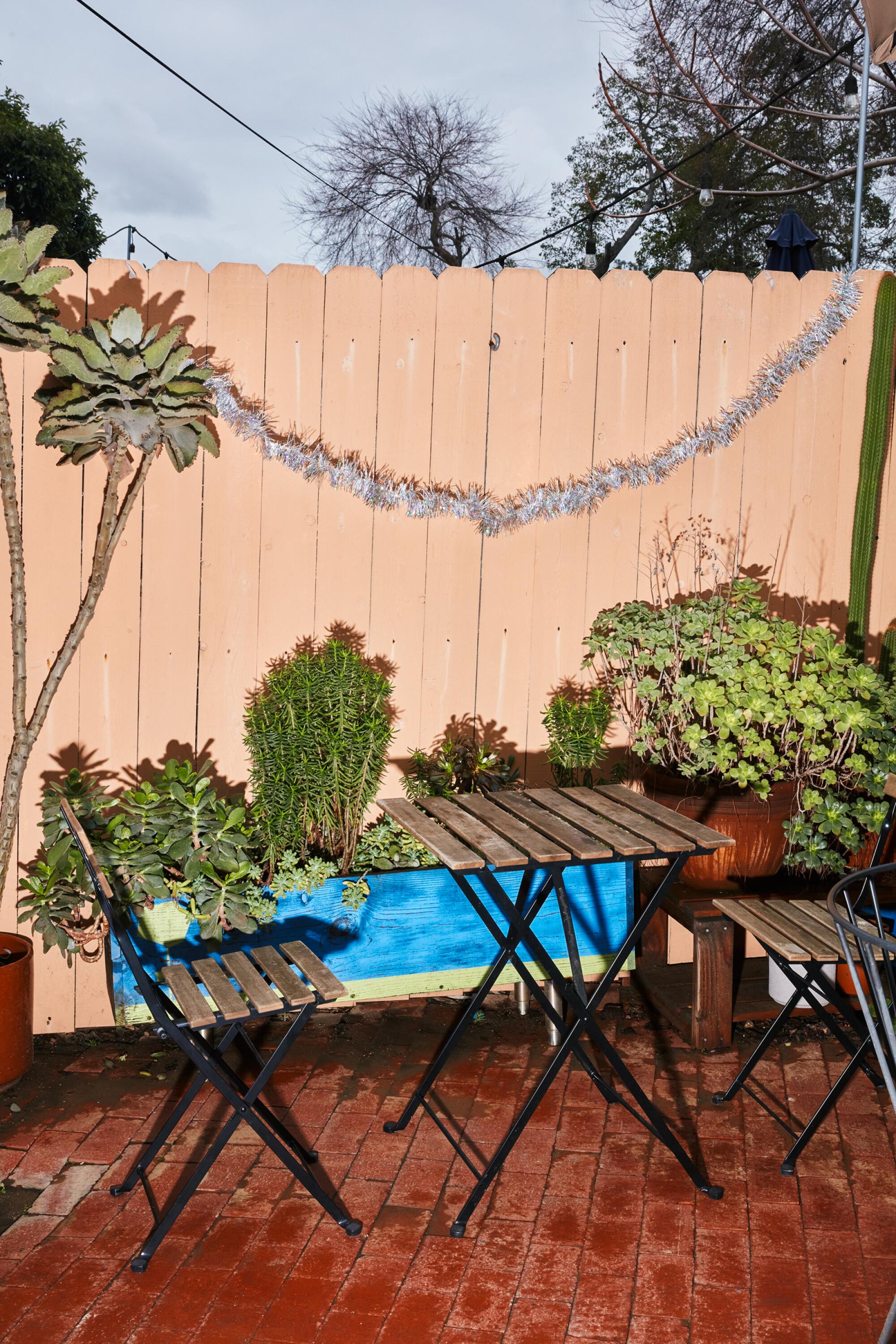 A cafe table and chairs outdoors, next to a wooden fence with potted succulents.