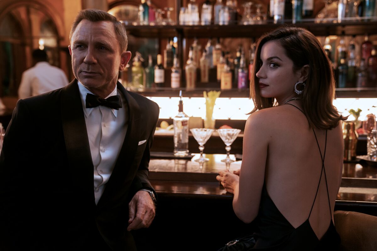 A man in a tux, left, and a woman in a cocktail dress at a bar