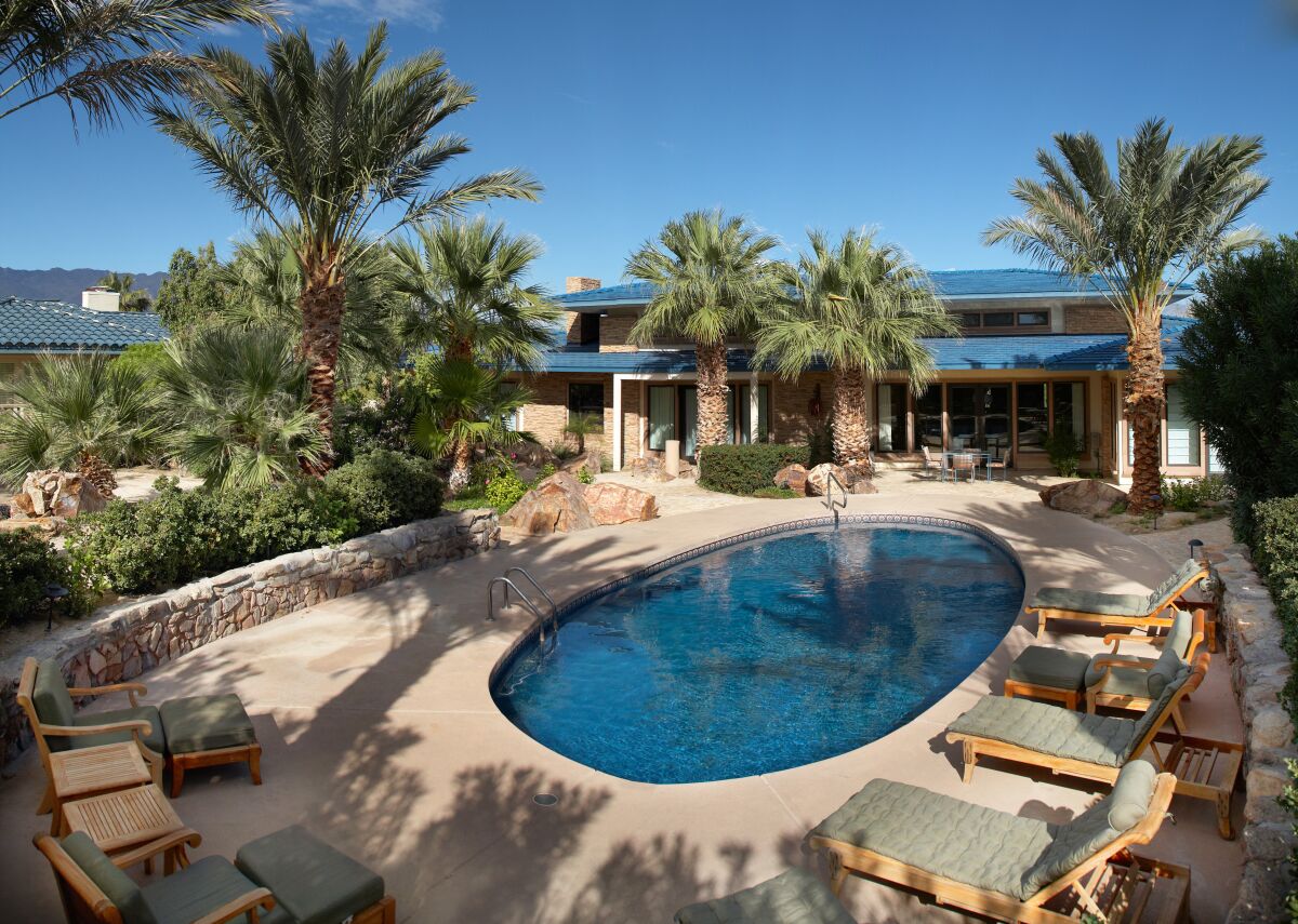 A large pool and palm trees outside a luxury home in the desert.