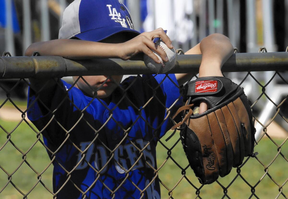 A young Dodgers fan slumps his glove over the fence while waiting to catch players' autographs during Dodgers spring training at Camelback Ranch in Glendale, Ariz.
