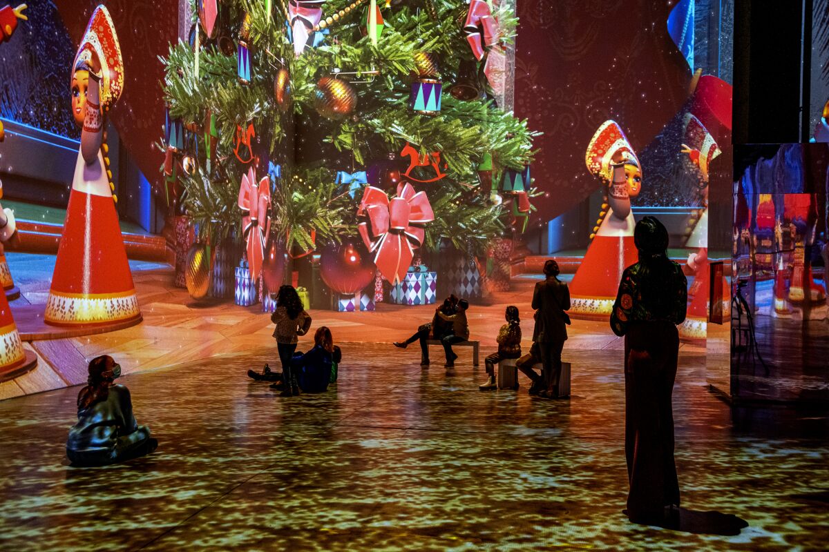A group of people looking around at large projections of a Christmas tree and animated toys.
