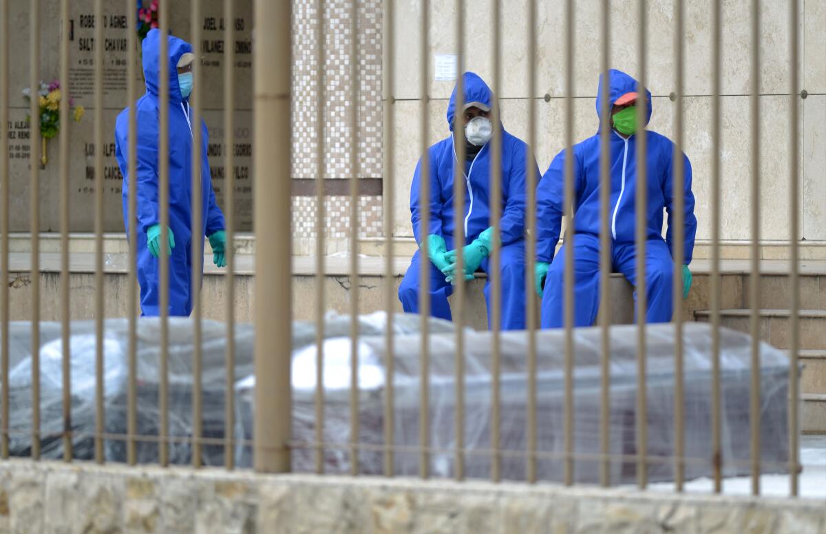 Workers in protective suits wait next to coffins in pandemic-stricken Guayaquil, Ecuador