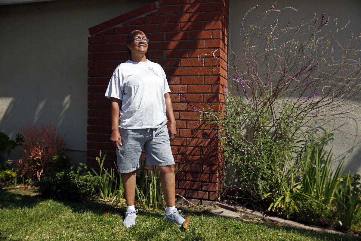A woman in shorts and a T-shirt stands on a lawn at the side of a house