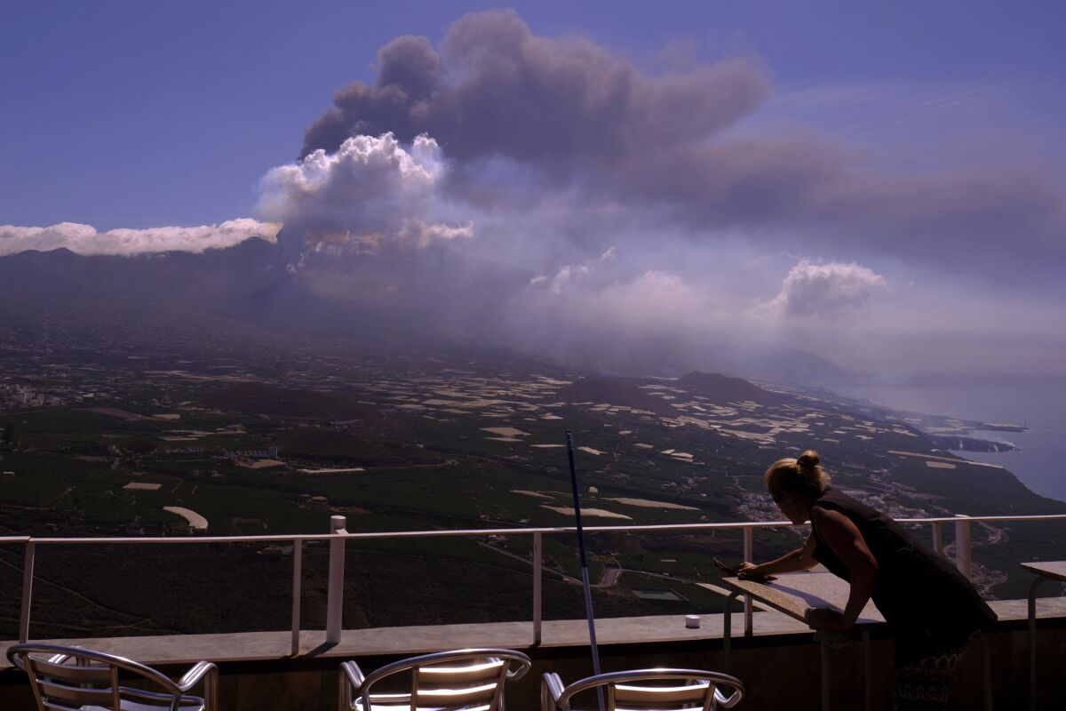 A worker cleans the ash from the tables of a restaurant as lava flows from a volcano on the Canary island of La Palma, Spain on Monday Oct. 4, 2021. More earthquakes are rattling the Spanish island of La Palma, as the lava flow from an erupting volcano surged after part of the crater collapsed. Officials say they don't expect to evacuate any more people from the area, because the fiery molten rock was following the same route to the sea as earlier flows. (AP Photo/Daniel Roca)
